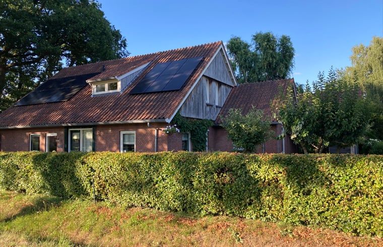 Zonnige gevel van Vakantiehuis in Oldenzaal, Twente, met zonnepanelen en groene heg voor duurzame charme.