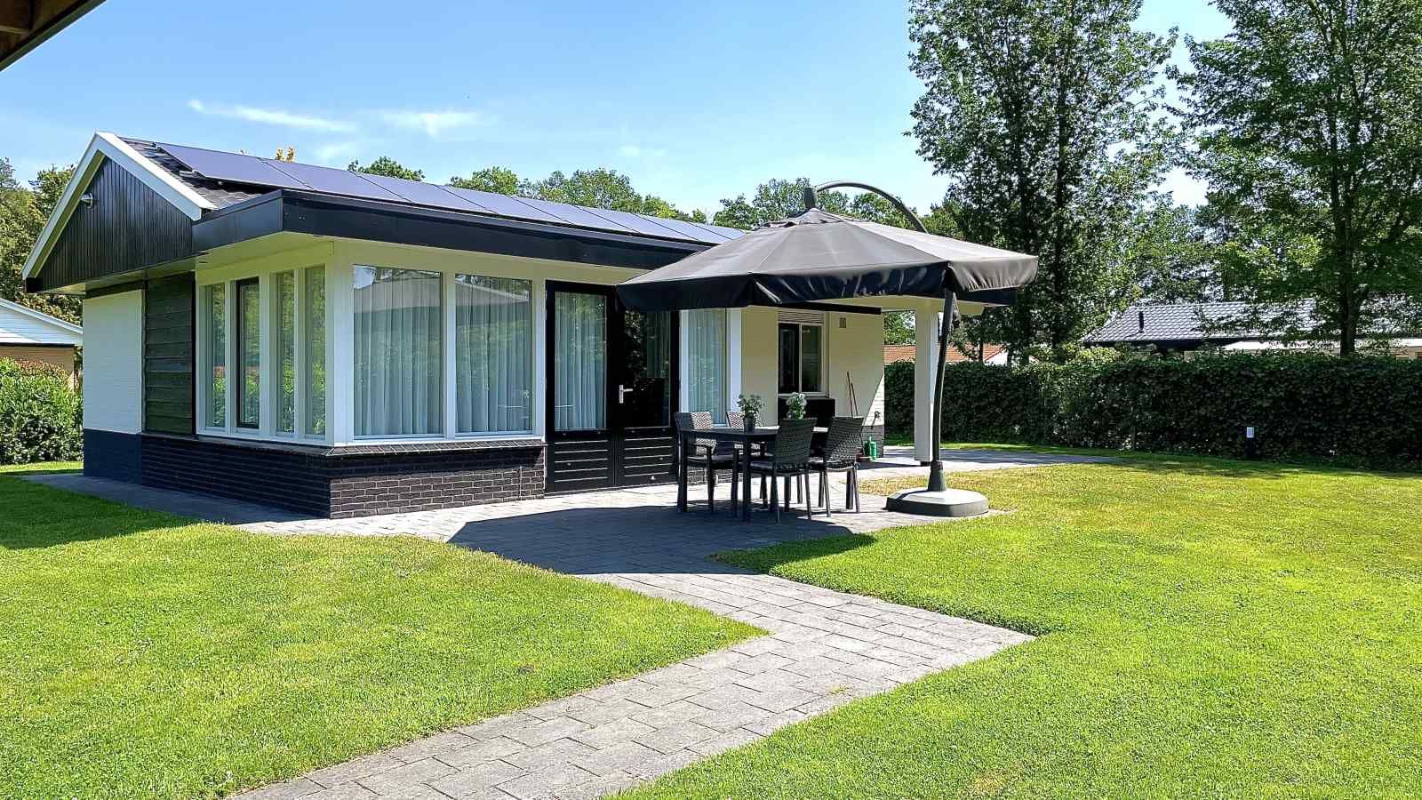 DG630 Ferienhaus in Denekamp, Twente mit sonniger Terrasse und Sonnenschirm auf gruenem Rasen.