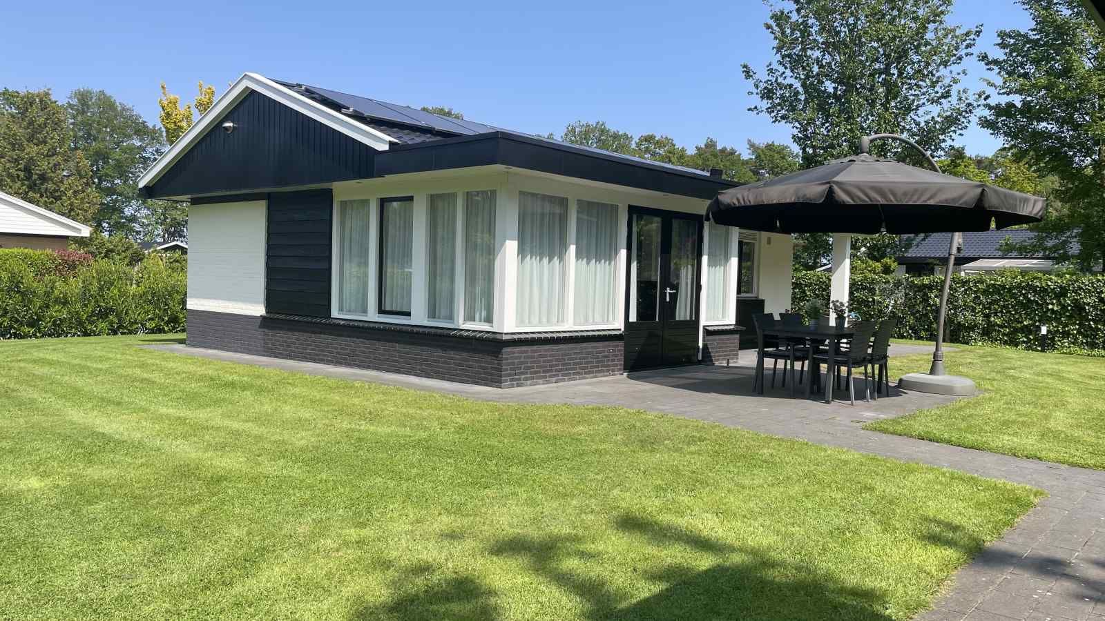 Sonnige Terrasse am Ferienhaus DG630 in Denekamp, Twente, mit Sonnenschirm und Gartenmoebeln.