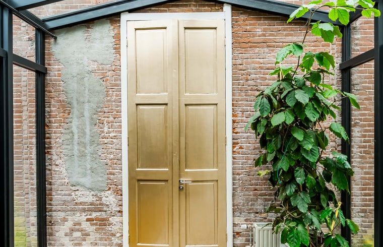 Charmante gouden deur in Vakantiehuis in Diepenveen, met een bakstenen muur en groene planten.