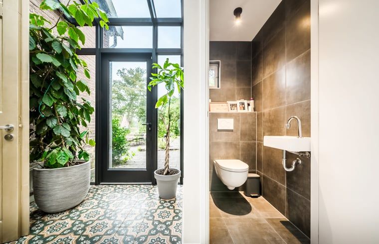 Entree van Vakantiehuis in Diepenveen met glazen deuren en kleurrijke tegels, omgeven door groen.