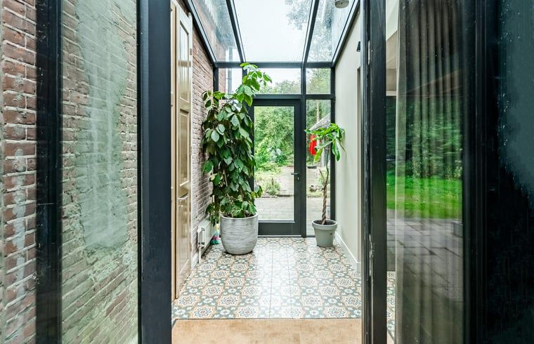 Glazen gang in Vakantiehuis in Diepenveen, met uitzicht op de tuin en stijlvolle tegelvloer in Overijssel.