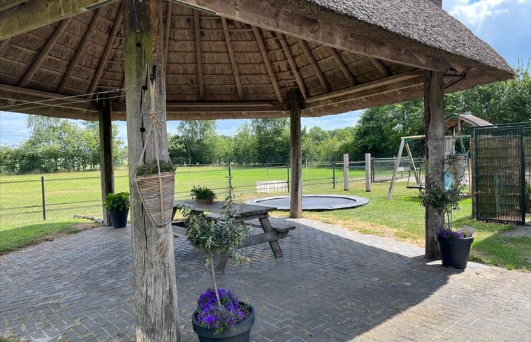 Offenes Gartenhaus im Ferienhaus in Beerze, Overijssel, mit Picknicktisch und Blick auf gruene Felder.