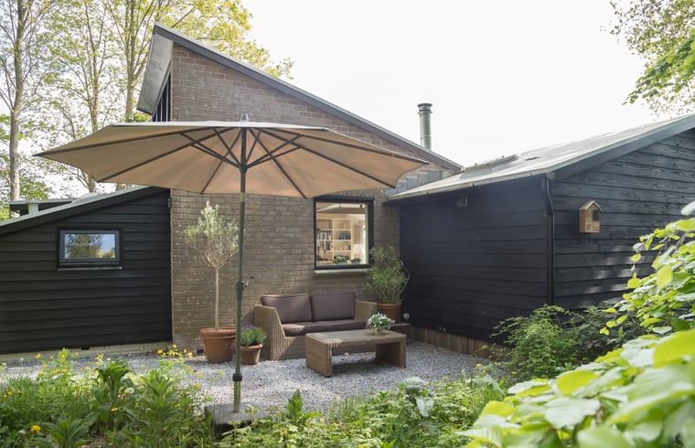 Schaduwrijke zithoek met parasol bij Vakantiehuisje in Stegeren, perfect voor warme dagen in Overijssel.