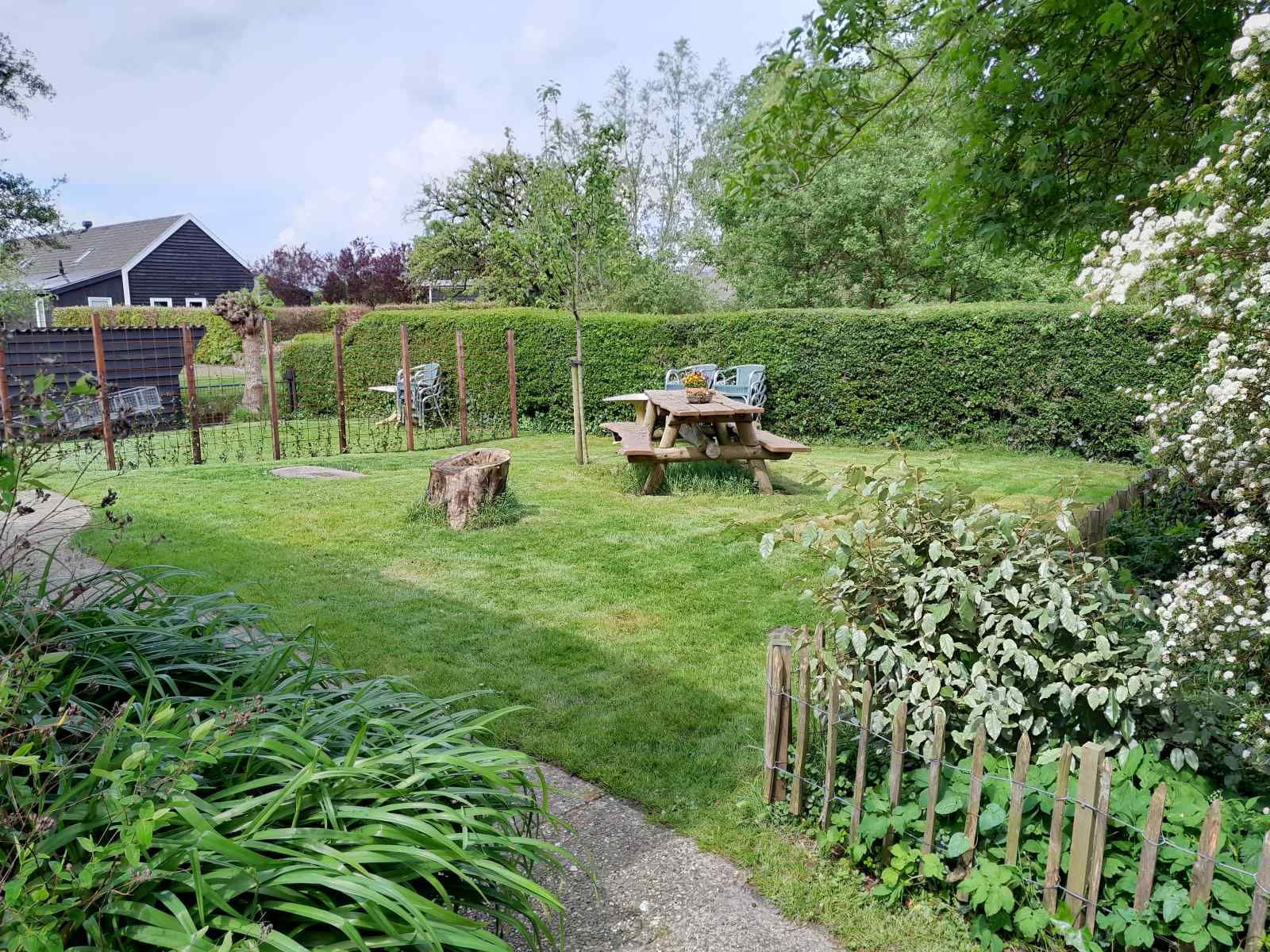Rustic garden of vacation home OV602 in Giethoorn with wooden picnic table and lots of greenery.
