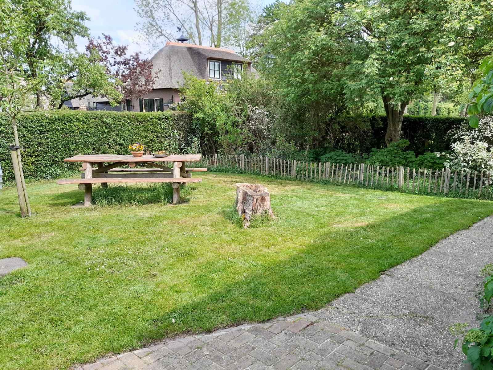 Shady garden of vacation home OV602 in Giethoorn with wooden picnic table.