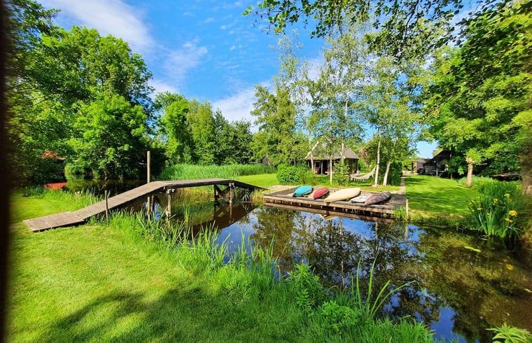 Ruhiges Wasser im Ferienhaus in Giethoorn, einem schoenen Ferienhaus in Overijssel, mit einer Holzbruecke und bunten Kissen.