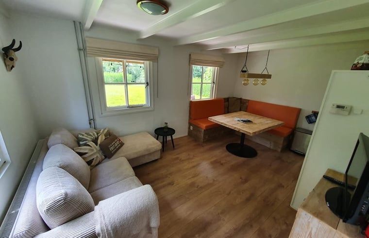 Helles Wohnzimmer im Ferienhaus in Giethoorn, Nordwest Overijssel, mit bequemem Sofa und grossen Fenstern mit Blick auf den Garten.