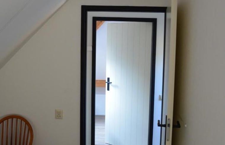 Helles Interieur eines Ferienhauses in IJhorst mit offener Tuer zum Schlafzimmer.