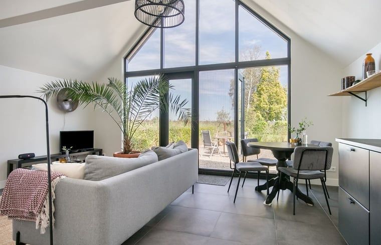 Lichte woonkamer van Vakantiehuis in Kalenberg, Overijssel, met grote ramen en uitzicht op de groene omgeving.