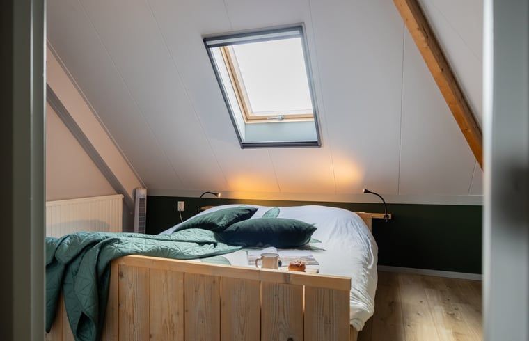 Sfeervolle slaapkamer in Vakantiehuisje in Wetering, Overijssel. Comfortabel bed onder een dakraam.