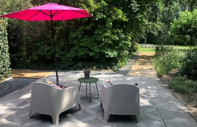 Zonnig terras bij Huisje in Tienhoven, vakantieaccommodatie in Tienhoven, Utrecht, met kleurrijke parasol en stoelen.