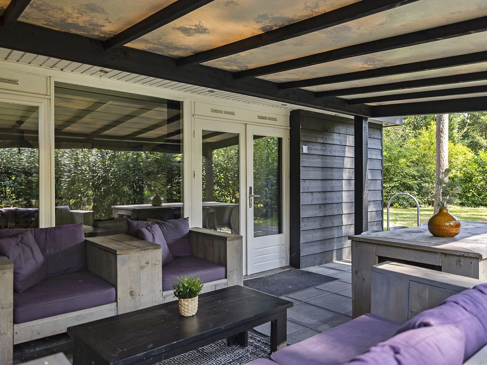 Entspannen Sie sich auf der ueberdachten Veranda des Bungalows Schoonoord in Doorn, Utrechtse Heuvelrug, mit Blick auf die gruene Umgebung.