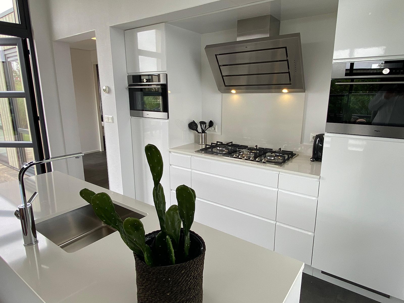 Modern kitchen in Chalet in Maarn, Utrechtse Heuvelrug, with sleek white cabinets and cooktop, ideal vacation home for a luxury stay.