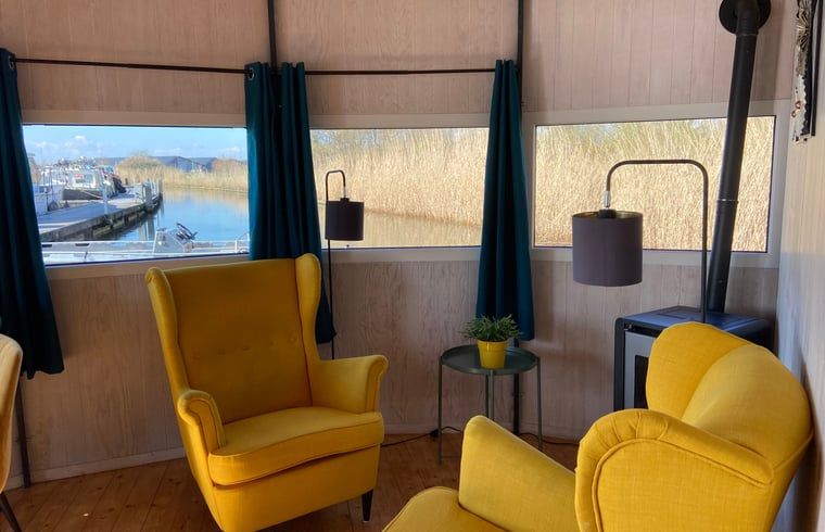 Cozy indoor area of Huisje in IJsselstein, vacation home located in Utrecht, with comfortable yellow armchairs and water views.