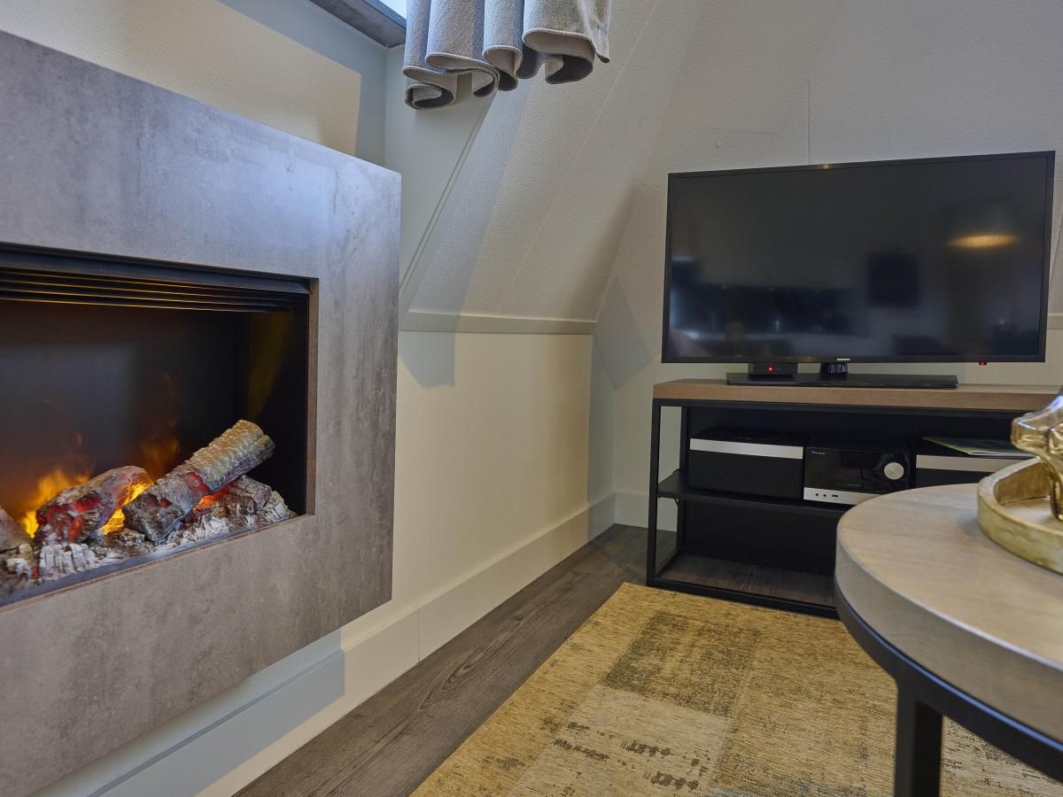 Cozy living room of Sauna Zee 27H in Colijnsplaat, North Beveland, with modern fireplace and flat-screen TV in the vacation home.