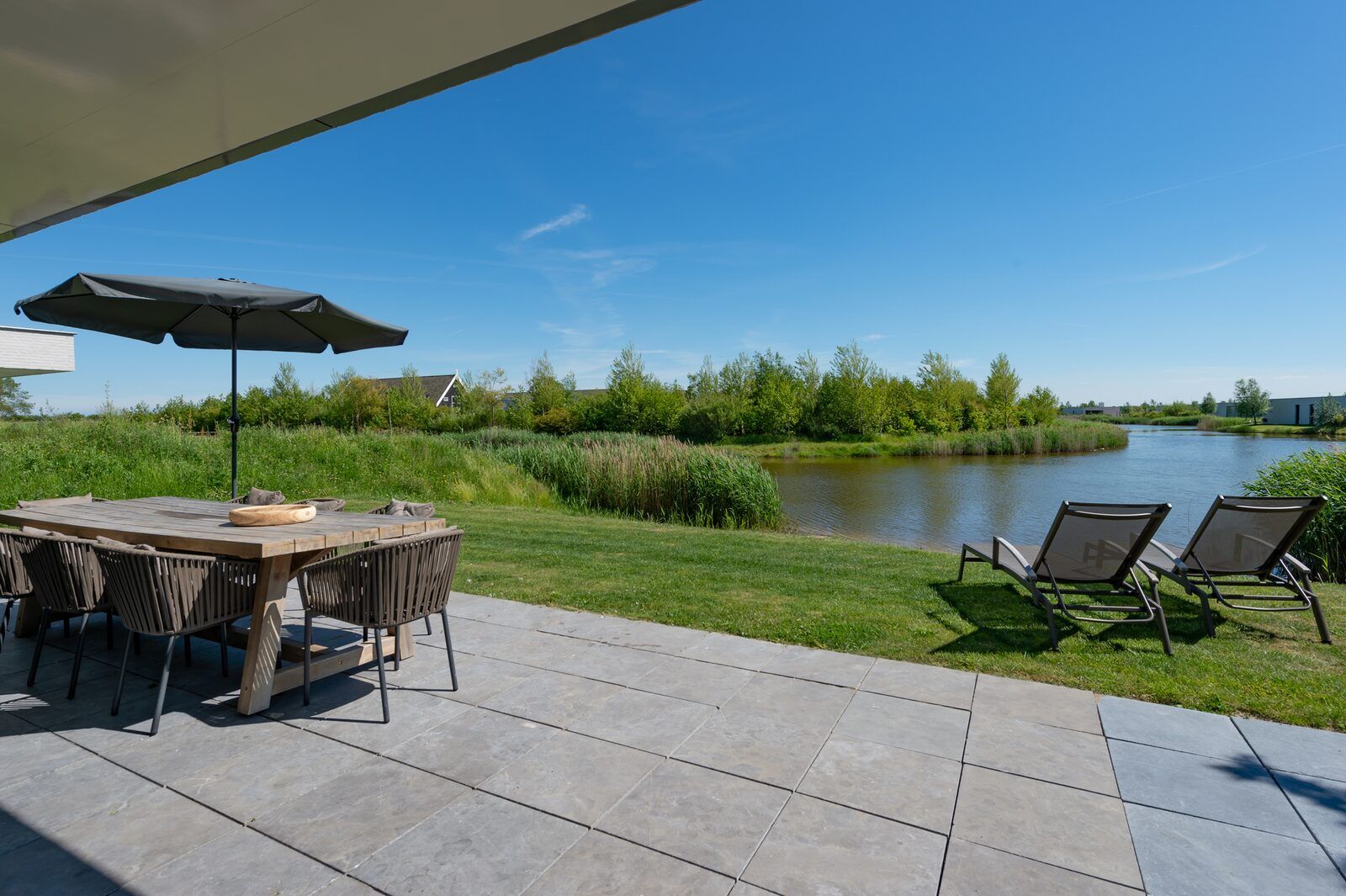 Ruime tuin met ligstoelen aan het water in Duinvallei 32, vakantiehuis in Kamperland, Zeeland.