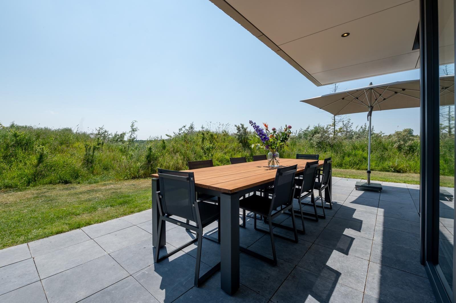 Zonnig terras van Duinvallei 39, De Groote Duynen, Kamperland, met een grote parasol en eettafel.
