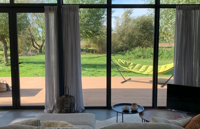 Blick vom Wohnzimmer des Ferienhauses Kamperland, mit Terrasse und gruener Umgebung in Zeeland.