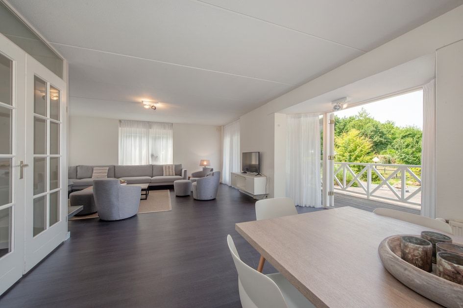 Geraeumiges Wohnzimmer der Villa R10B in Kamperland, Noord-Beveland, Zeeland mit moderner Einrichtung und Blick auf die gruene Umgebung.