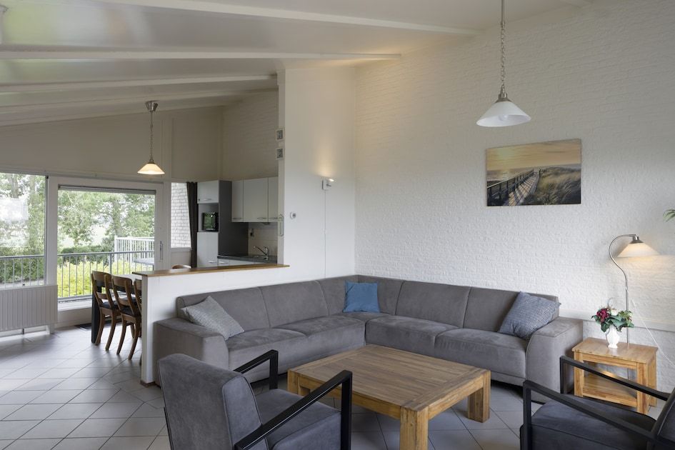 Gemuetliches Wohnzimmer im Bungalow BE, Kamperland, Noord-Beveland, Zeeland mit geraeumiger Sitzecke und Blick auf die gruene Umgebung.