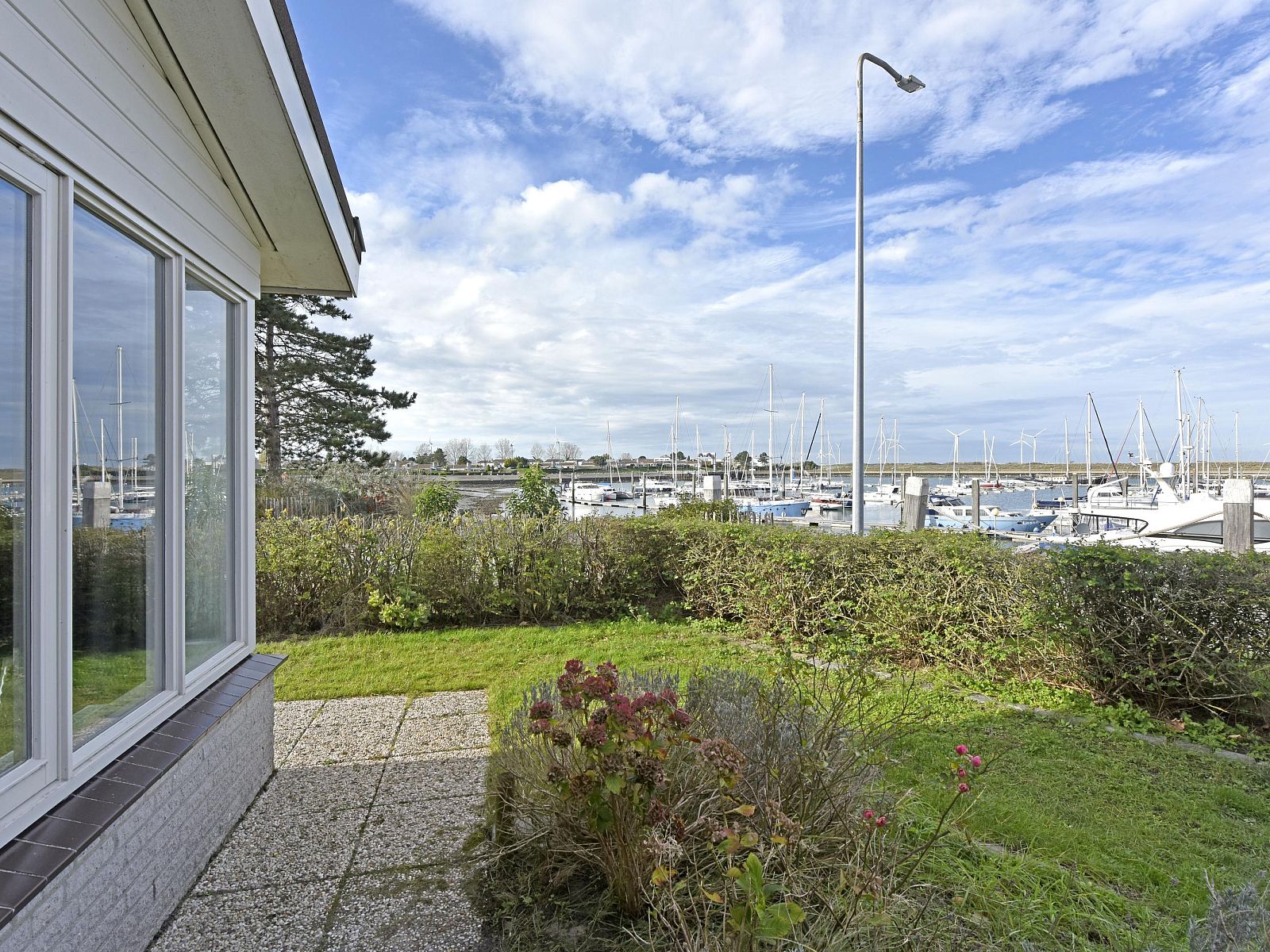 Blick auf den Yachthafen vom Einfamilienhaus in Kamperland, Ferienhaus in Noord-Beveland, Zeeland mit grnem Garten und blauem Himmel.