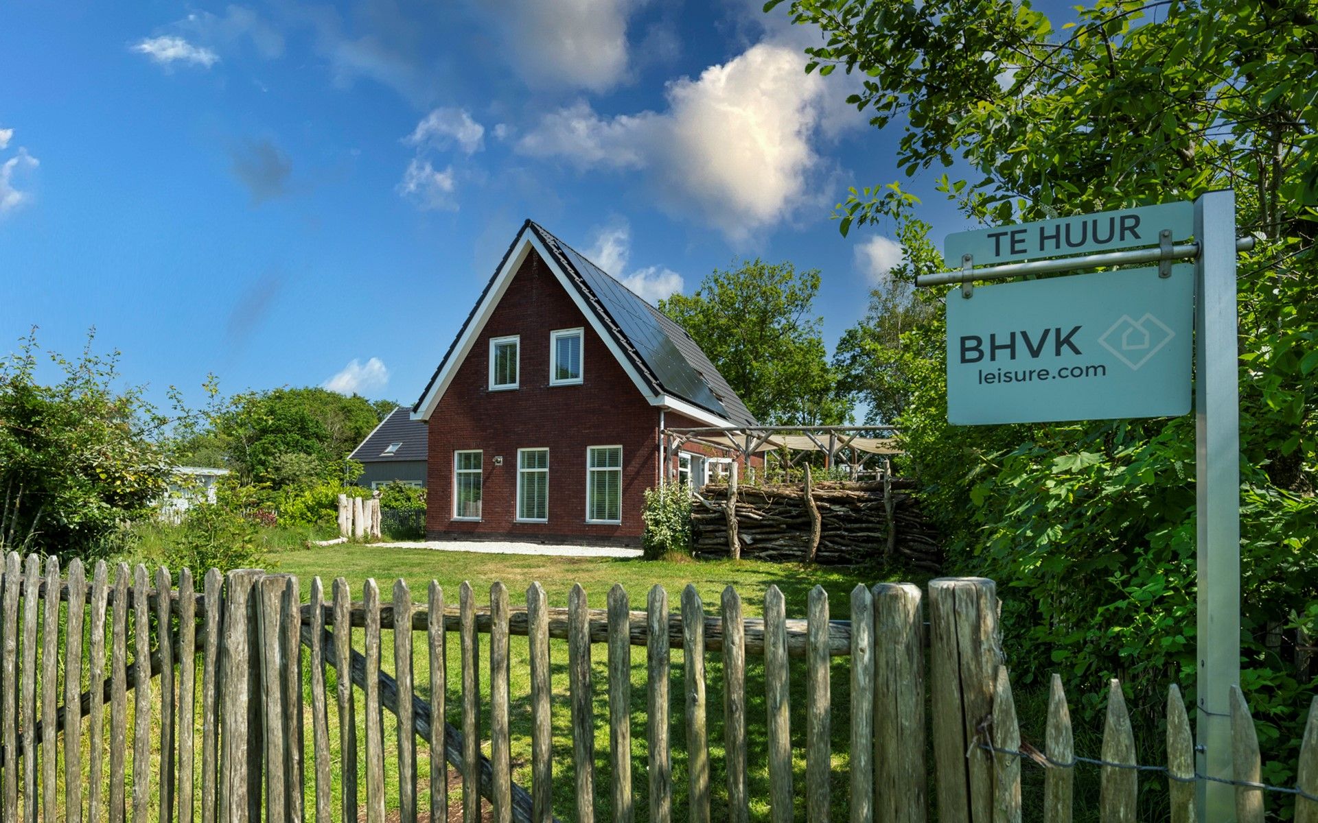 Ferienhaus De Zuidhoek 6 in Renesse, eingezaeunt mit Holzzaun und gruener Umgebung.