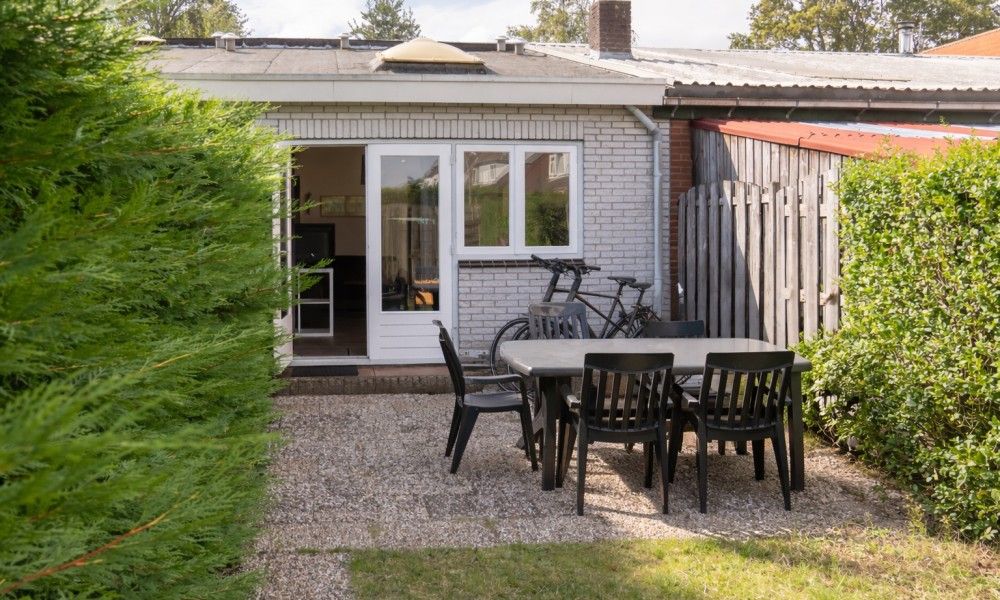 Veranda von 3 in einer Reihe Ferienhaus in Renesse, Schouwen-Duiveland, Zeeland mit Gartenmoebeln und gruener Umgebung.