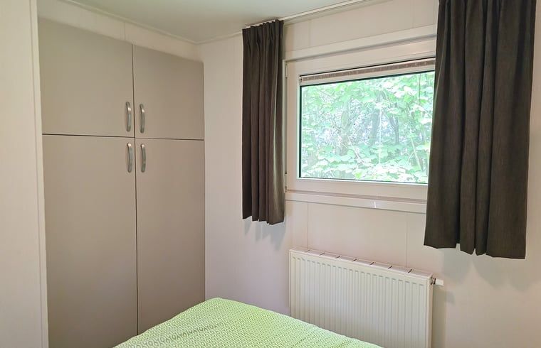 Slaapkamer in Huisje in Oostkapelle, Walcheren, met kledingkast en tuinzicht.