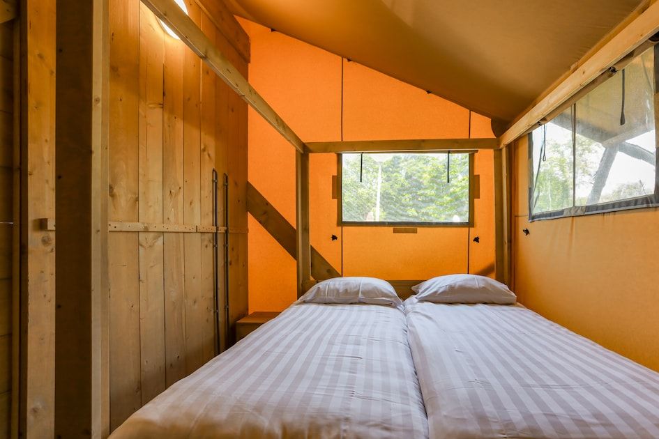 Gemuetliches Schlafzimmer in Safaritent 8, einer Glamping-Lodge in Vrouwenpolder, Walcheren, Zeeland, mit Holzakzenten und natuerlichem Licht.