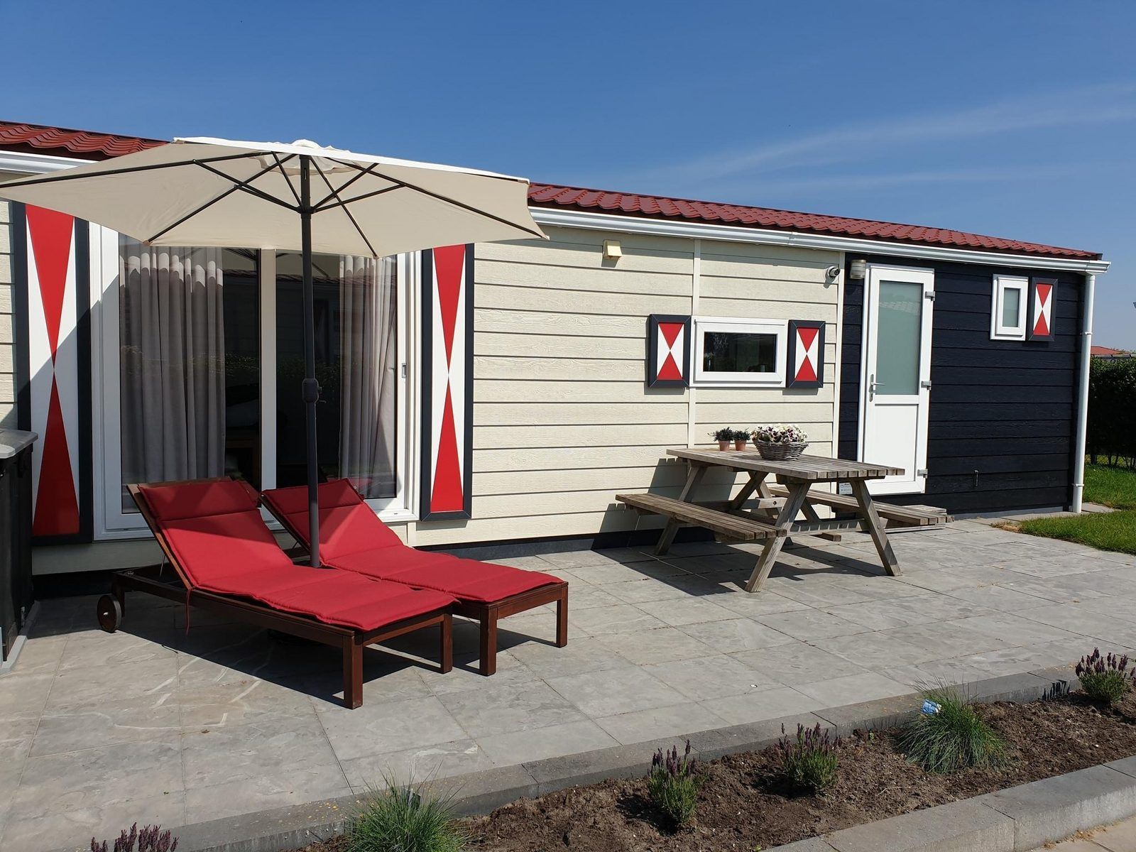 Terrasse von VZ816 Chalet in Veere, Serooskerke, Walcheren, mit Picknicktisch und Sonnenschirm.