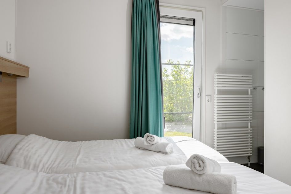 Lichte slaapkamer van Lodge 4B in Breskens, Zeeland, met toegang tot eigen badkamer en uitzicht op de tuin.