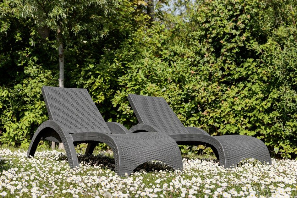 Zonnige ligstoelen in de tuin van Lodge 4B, Breskens, Zeeland, omgeven door bloeiende bloemen en groen.