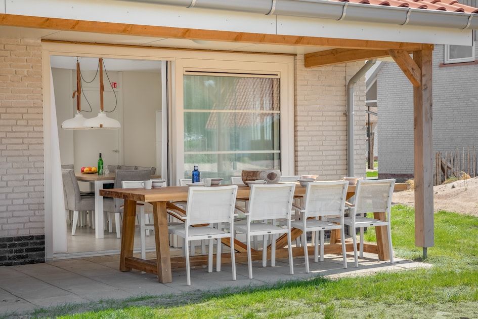 Geraeumige Terrasse des V8 Luxus-Ferienhauses in Nieuwvliet-Bad, Zeeland, mit komfortablen Essmoeglichkeiten.