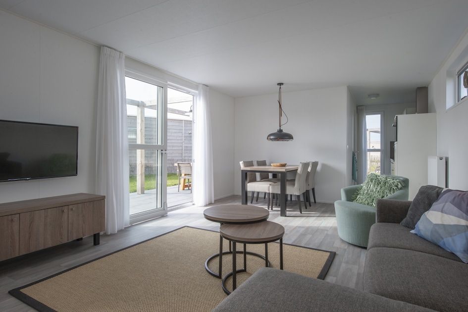 Modernes Wohnzimmer im Ferienhaus L4 Comfort, Nieuwvliet-Bad, Zeeland, mit heller Einrichtung und Zugang zur sonnigen Terrasse.