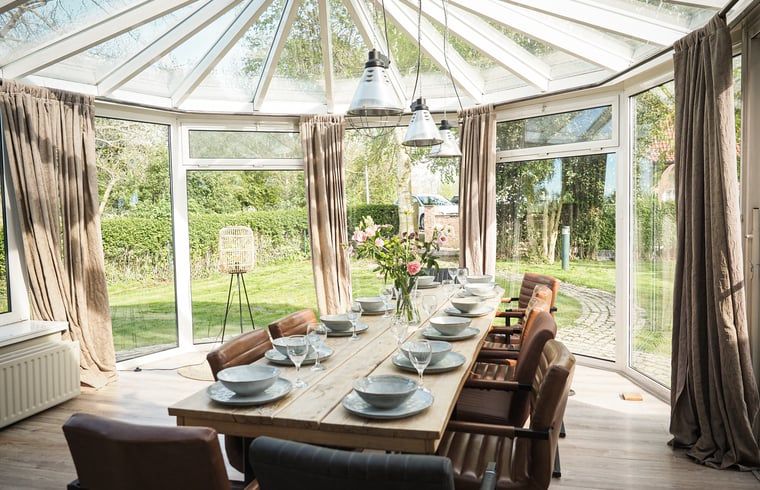 Lichte eetkamer in Vakantiehuis in Sluis, Zeeuws-Vlaanderen, met uitzicht op groene tuin. Perfect voor een ontspannen verblijf in Zeeland.