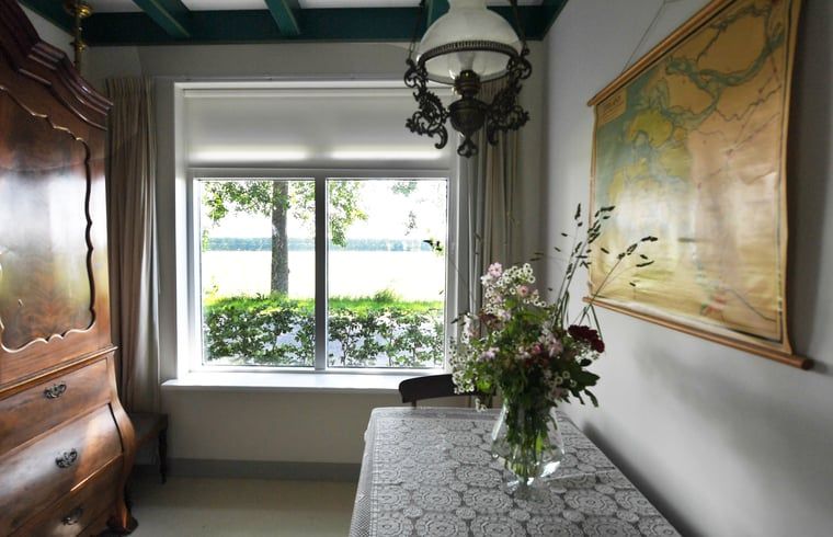 Binnenruimte van Vakantiehuisje in Lewedorp, Zuid-Beveland, met uitzicht op de natuur. Gezellige inrichting met bloemen en kaart aan de muur.