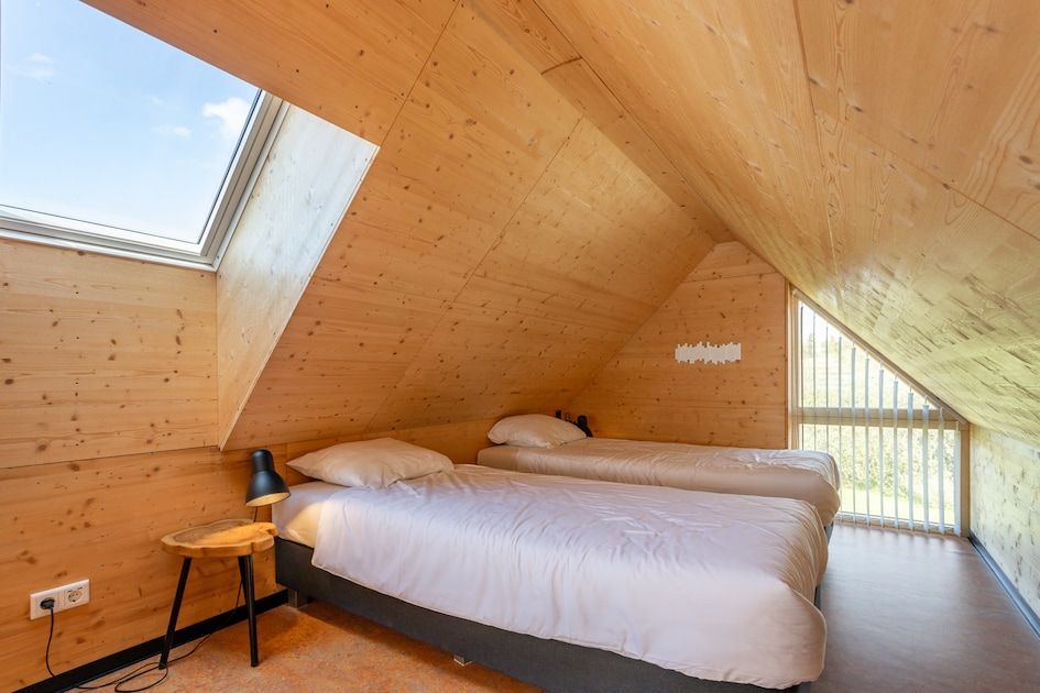 Gezellige slaapkamer in ECO Cottage, een vakantiehuis in Ouddorp, Goeree-Overflakkee, met houten interieur en dakraam voor natuurlijk licht.