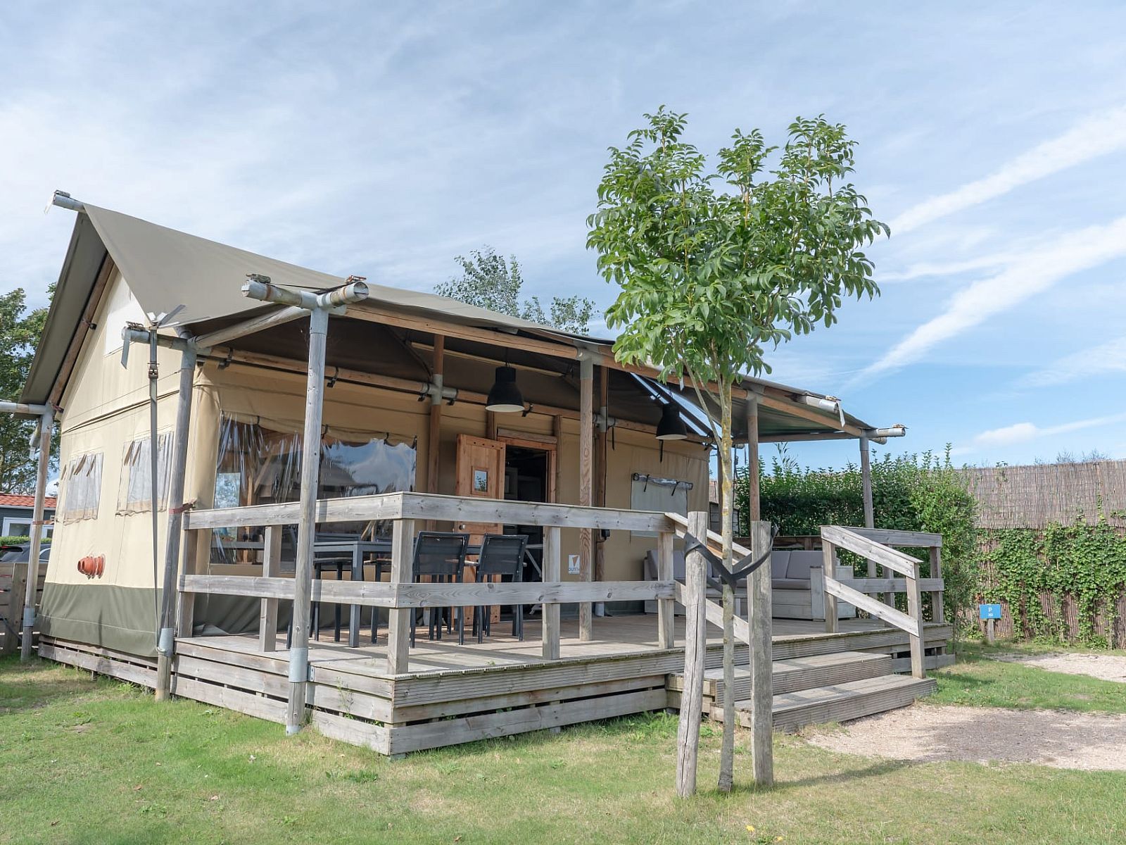 Veranda des Safarizeltes Duinroos in Ouddorp, einer Glamping Lodge in Goeree-Overflakkee, Suedholland, umgeben von gruener Natur.
