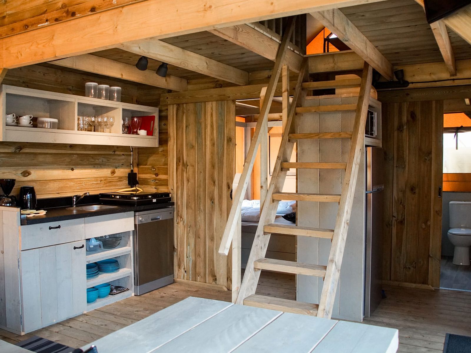 Gemuetlicher Innenbereich des Safarizeltes Duinroos in Ouddorp, Goeree-Overflakkee, mit Holzinterieur und moderner Kuecheneinrichtung.