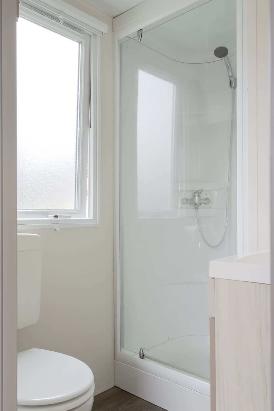 Modernes Badezimmer im Mobil home de Aalscholver, Mobil home in Ouddorp, Goeree-Overflakkee, Suedholland, mit eleganter Dusche und Fenster.