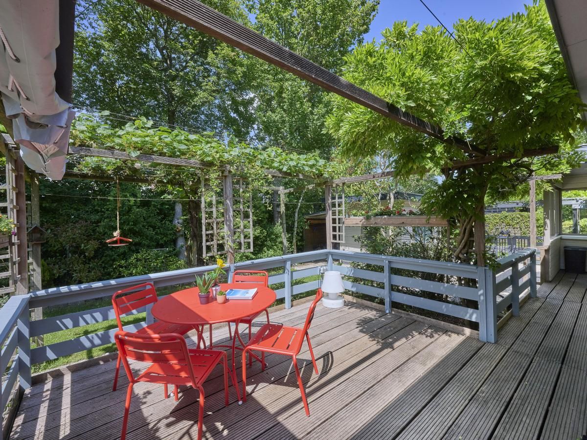 Veranda von Huisje Joep in Goedereede, schoene Terrasse mit roten Stuehlen, umgeben von Natur.