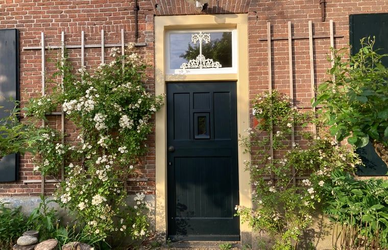 Charmanter Eingang zum Ferienhaus in Balgoij, Rijk van Nijmegen, Gelderland, umgeben von bluehenden Schlingpflanzen und historischen Backsteinen.