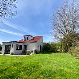 Vakantiehuis D 491 in De Cocksdorp, Texel, biedt een prachtig uitzicht op een groene tuin en blauwe lucht, ideaal voor een ontspannen verblijf.