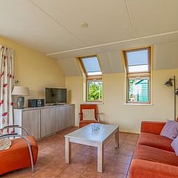 Lichte woonkamer in Vakantiehuisje in De Cocksdorp, Texel met comfortabele zithoek en uitzicht op de tuin, ideaal voor ontspanning.