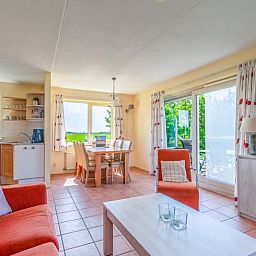 Lichte woonkamer van Vakantiehuisje in De Cocksdorp, Texel met uitzicht op groene natuur en ruime eethoek, ideaal voor ontspanning.