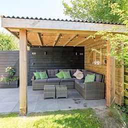 Ontspannen zithoek op het terras van Vakantiehuis A 103 in De Cocksdorp, Texel, met comfortabele loungebank en groene kussens.