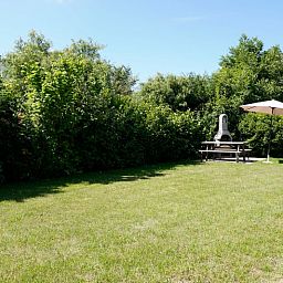 Spacious garden at Holiday home D 669 in De Cocksdorp, Texel with green surroundings and terrace with parasol, ideal for relaxation on the Wadden Islands.
