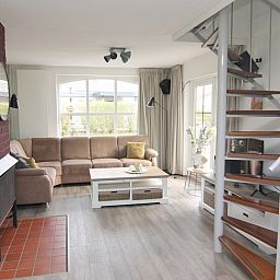 Gezellige woonkamer in Vakantiehuis E 632, De Cocksdorp, Texel, met comfortabele zithoek en wenteltrap, ideaal voor ontspanning.