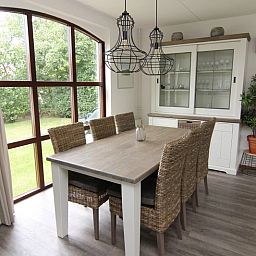 Gezellige eetkamer in Vakantiehuis E 632, De Cocksdorp, Texel met uitzicht op de groene tuin en moderne inrichting.